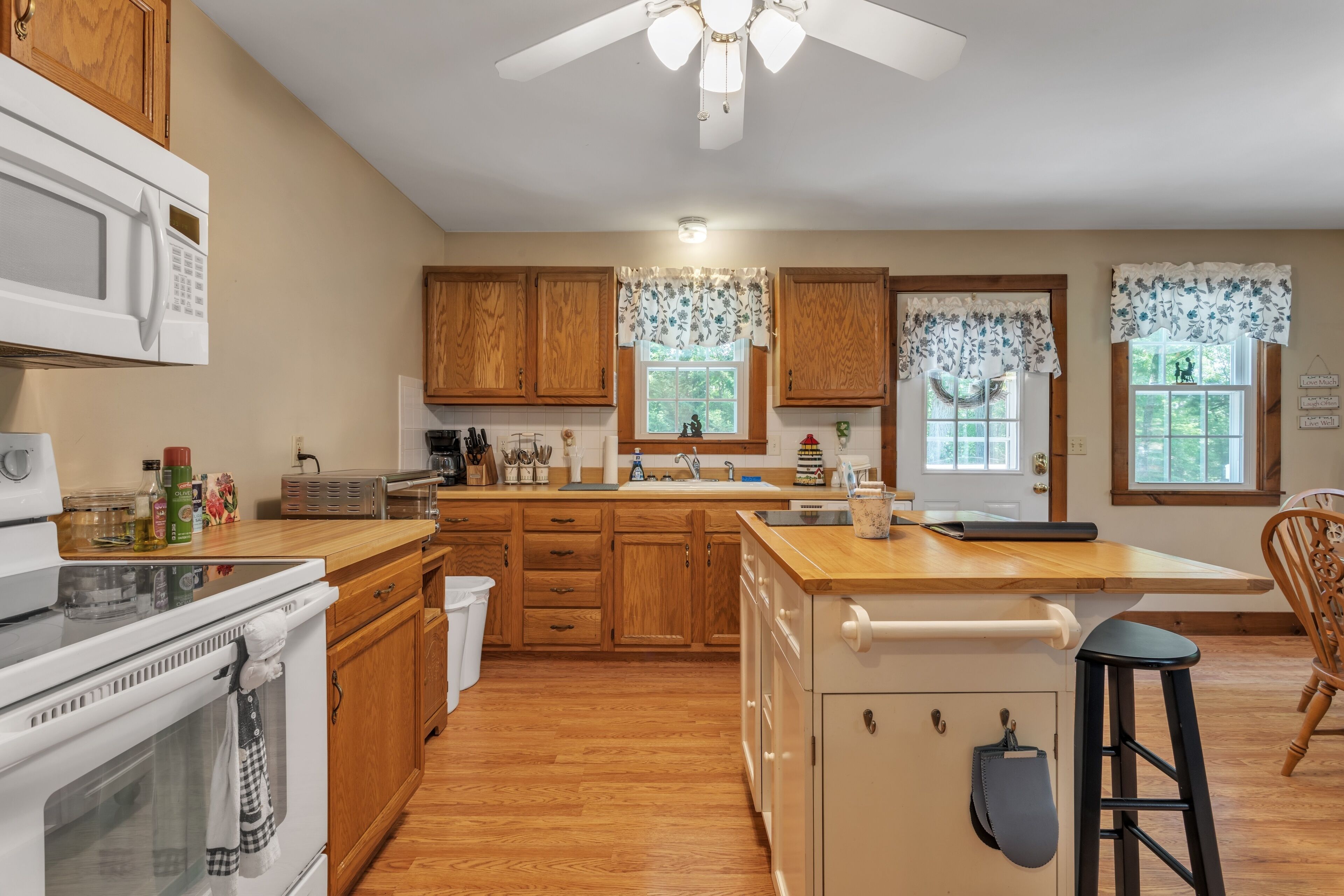 A kitchen with wooden cabinets, a white stove, a microwave, and a wooden island with a sink.