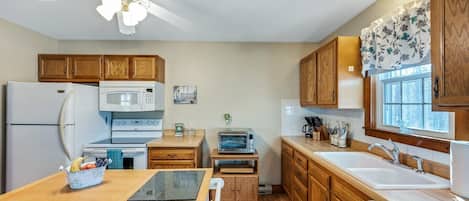 A kitchen with wooden cabinets, a refrigerator, microwave, oven, and a window with a view.
