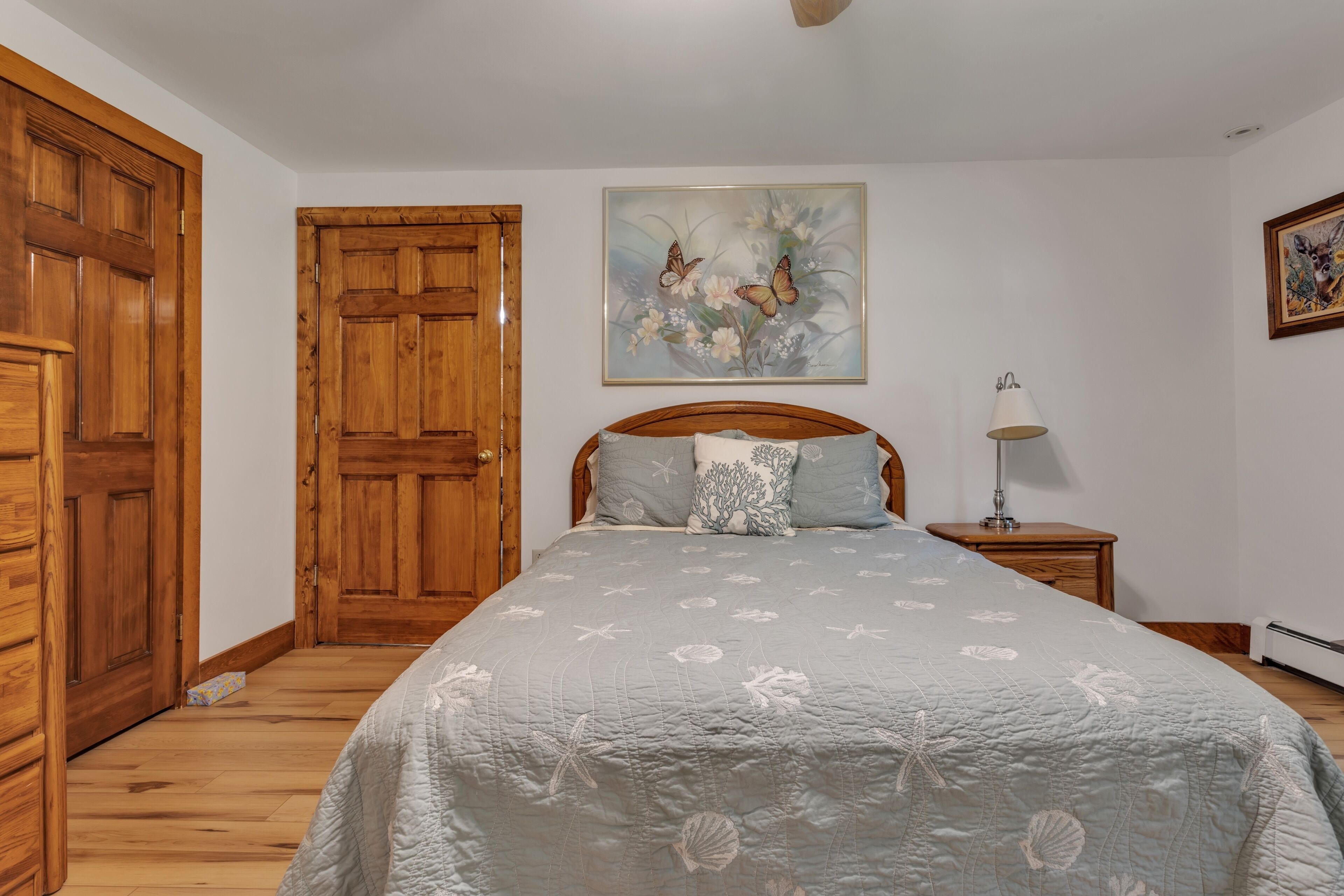 Un dormitorio con cama de madera, una mesita de noche con lámpara, un cuadro en la pared y una puerta de madera.