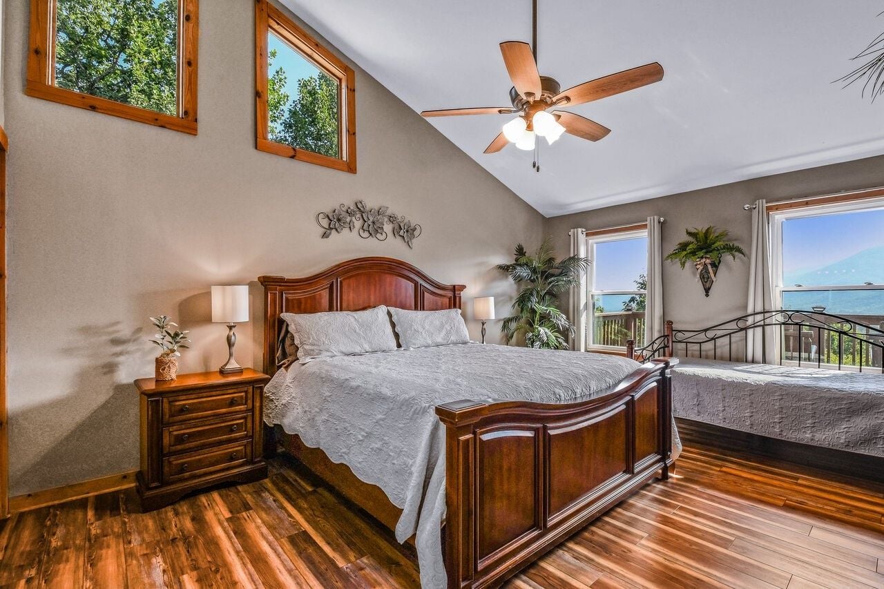 A bedroom with a wooden bed, a ceiling fan, and a balcony with a view.