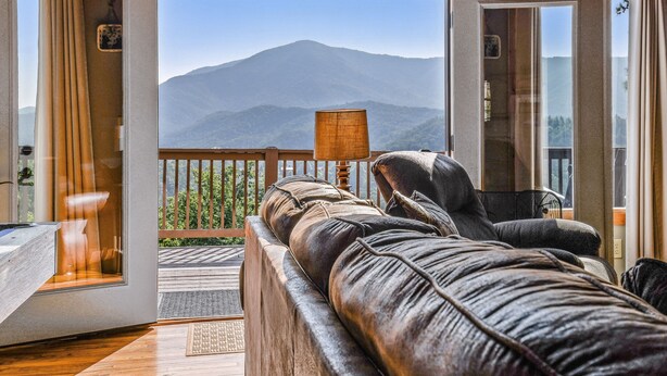A room with a leather sofa facing a balcony with a mountain view. - Roundtop Mountain Ridge 2 Bedroom Cabin by RedAwning (Sevierville)