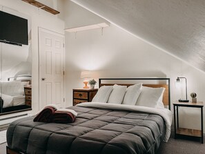 Un dormitorio con cama, mesitas de noche, lámpara y espejo.