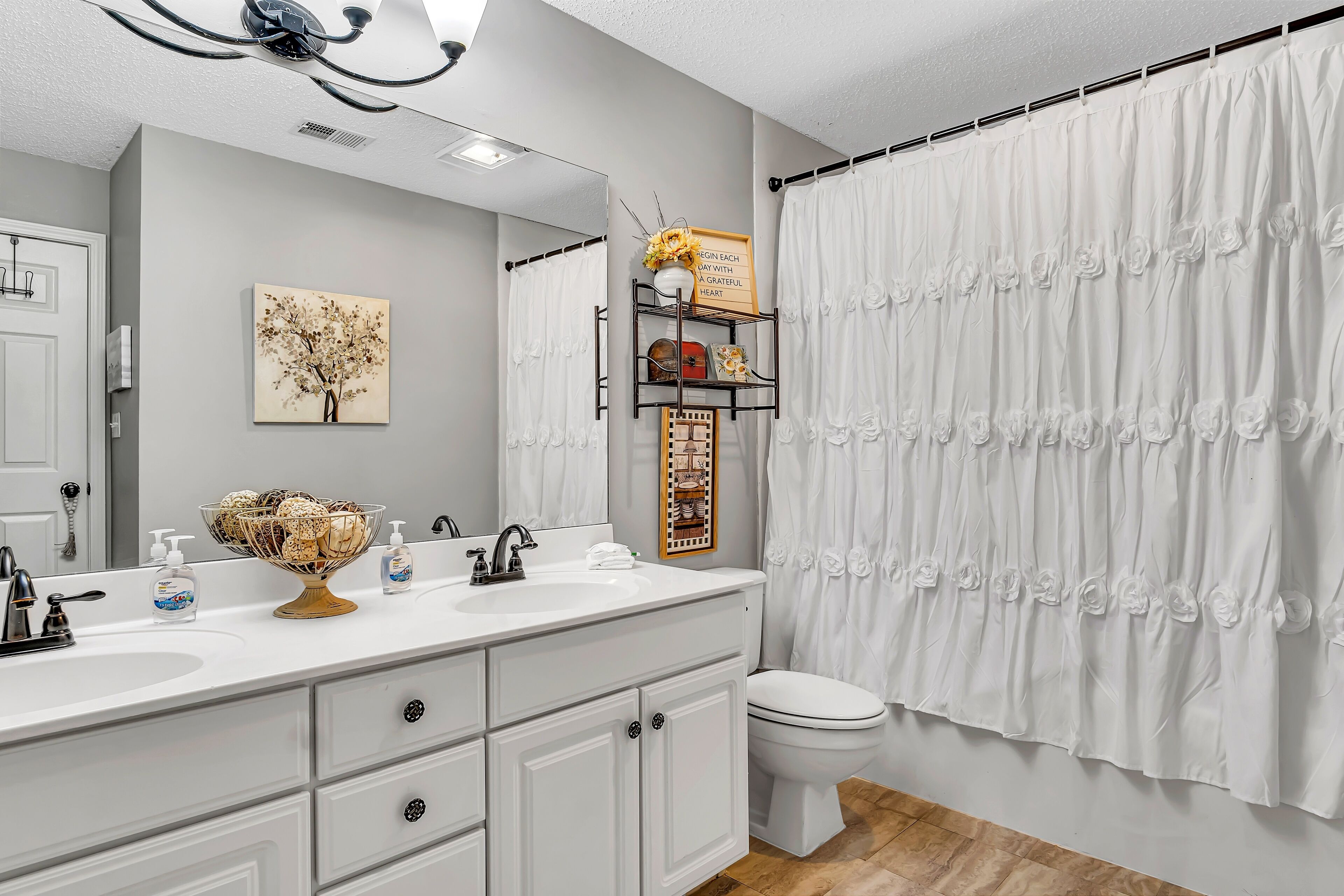 A bathroom with a white vanity, a sink, a mirror, a toilet, and a shower curtain.