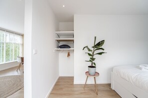 A bedroom with a bed, a potted plant, a window, and a closet with shelves. - The Shell Apartment 59 (Zandvoort)