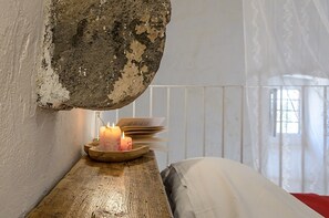 Una mesa de madera rústica con velas y un libro, un muro de piedra y una ventana con vistas.