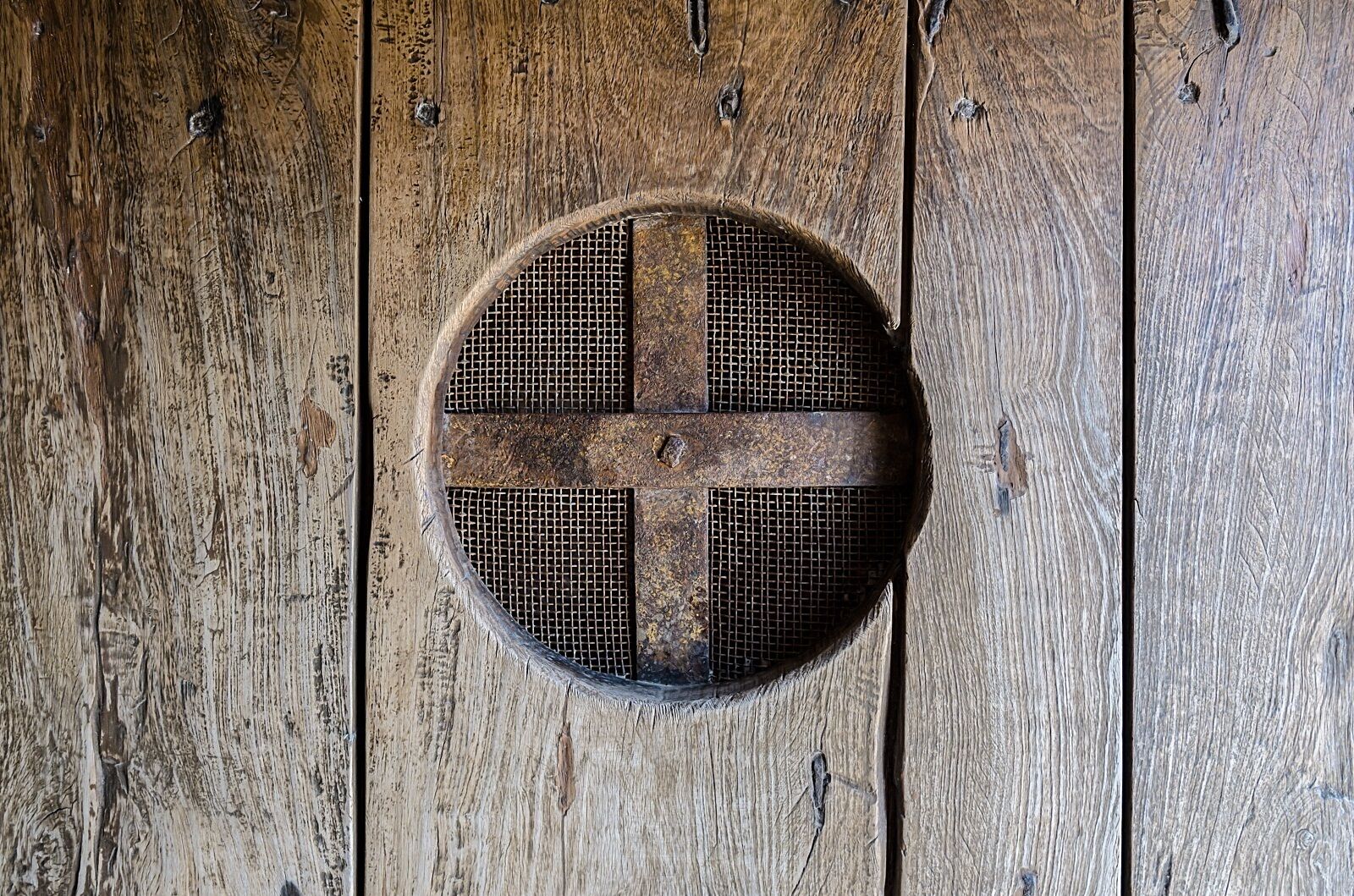 A circular metal grate with a cross design, mounted on a wooden surface.