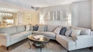 A modern living room with a L-shaped sectional sofa, a glass coffee table, and a decorative wall piece.