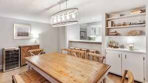 Ein Essbereich mit Holztisch und Stühlen, einer Chandelieber, einem weißen Schrank mit Dekorationen und einer Küchenzeile im Hintergrund.