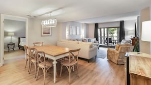 A spacious living area with a wooden dining table, a sofa, and a balcony with a view.