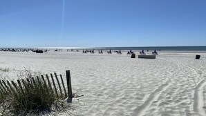 Ein weiter Sandstrand mit Reihen von Liegestühlen und Sonnenschirmen, ein Holzzaun im Vordergrund und das Meer im Hintergrund.