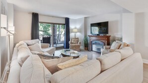 Ein modernes Wohnzimmer mit einer Sofagarnitur, einem Kamin, einem Fernseher und einem Balkon mit Vorhängen.