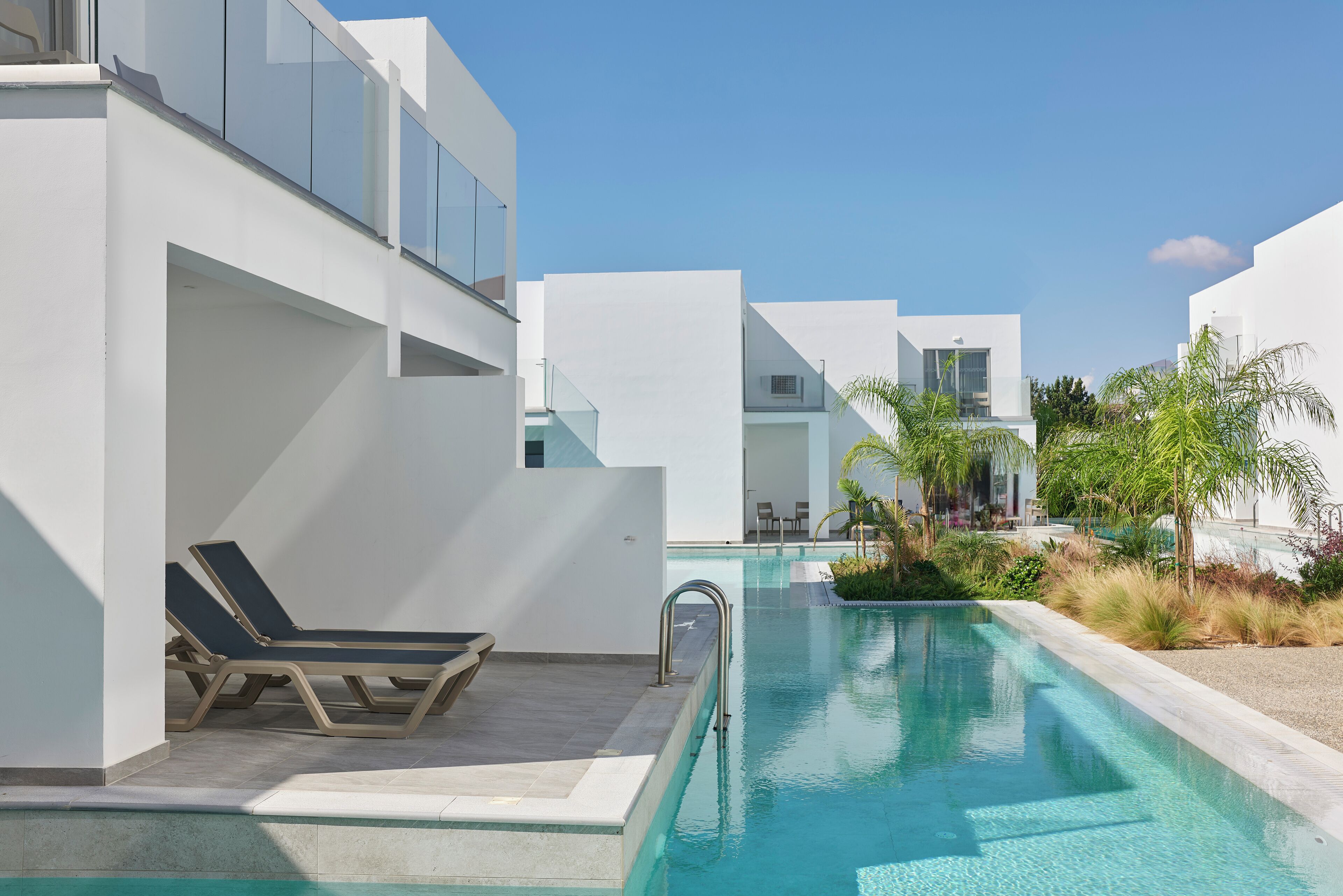 A modern pool area with lounge chairs, a clear pool, and white buildings.