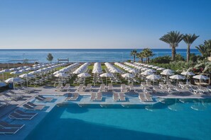 A pool area with sun loungers and umbrellas, a clear blue sky, and the ocean in the background.