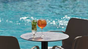 Una mesa con dos bebidas junto a una piscina.