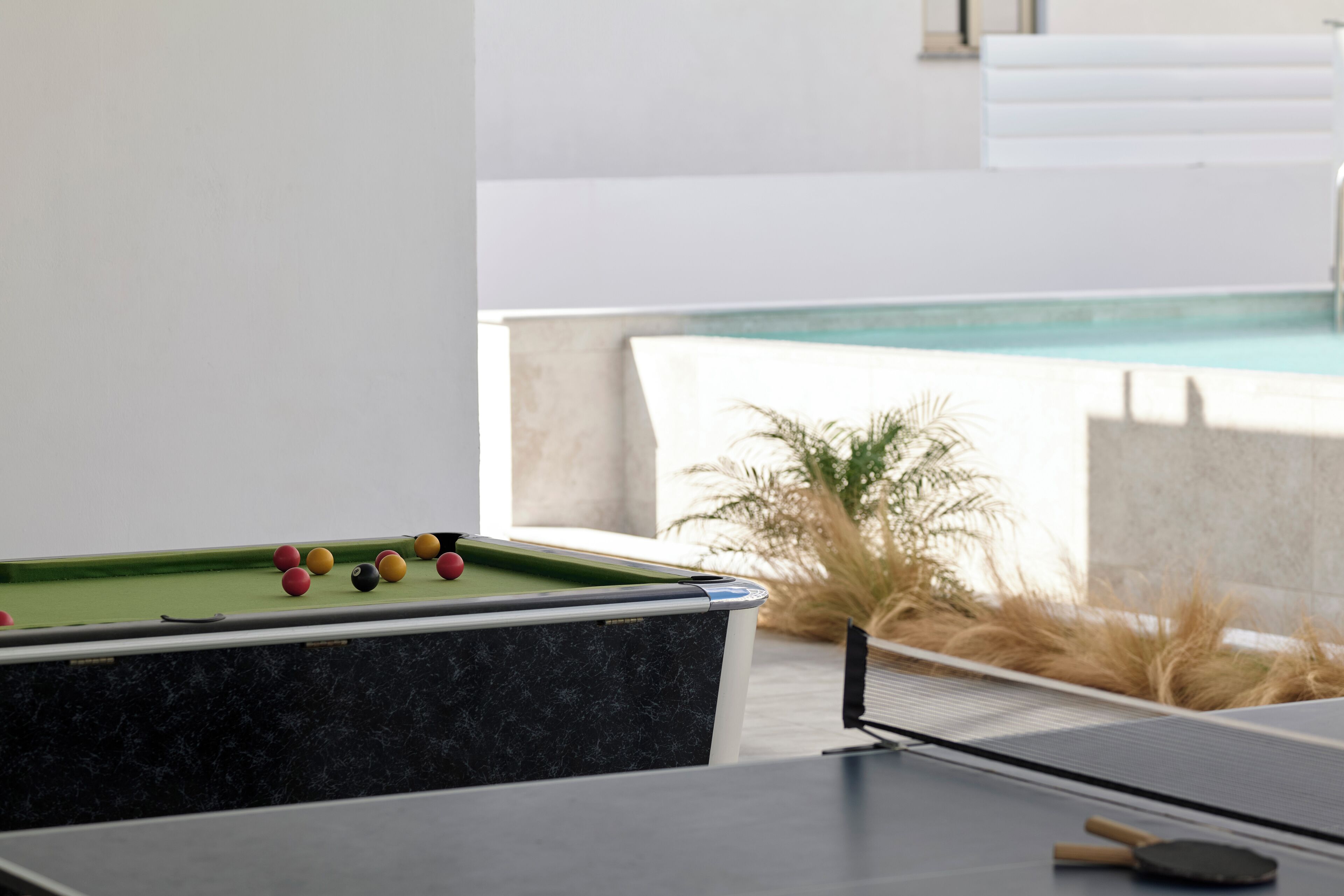 Une table de billard avec ses queues et ses billes, une table de ping-pong et une vue sur une piscine.