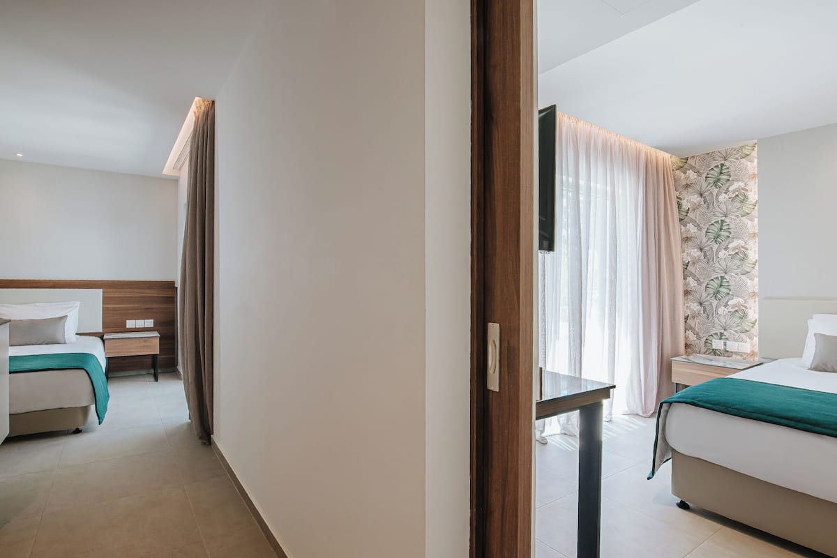 Habitación de hotel con cama, mesita de noche, espejo y ventana con cortinas.