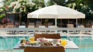 Ein Esstisch mit verschiedenen Speisen und Getränken am Pool, umgeben von Liegestühlen und einem Sonnenschirm.