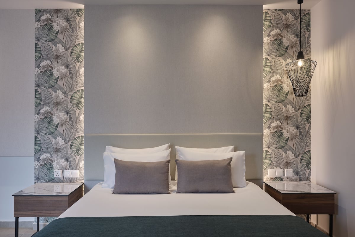 Un dormitorio moderno con una cama grande, dos mesitas de noche, una lámpara de pared y un papel tapiz tropical.