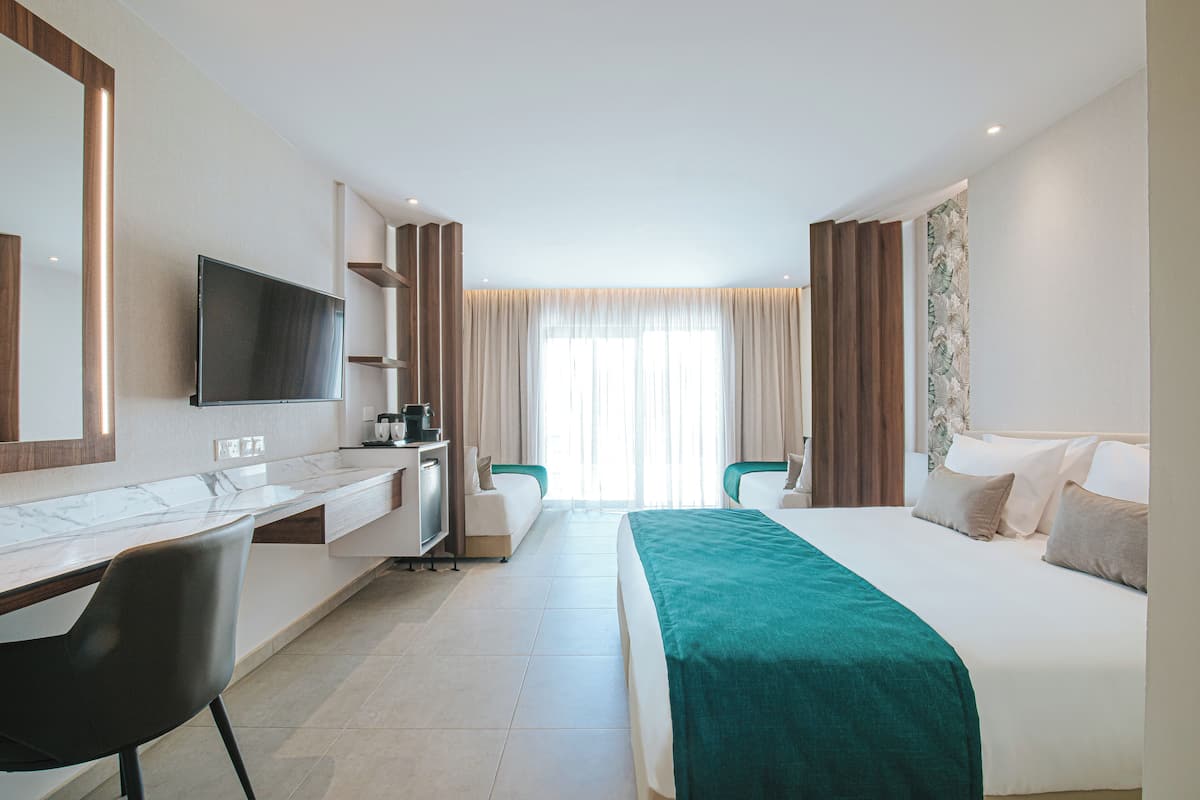 Habitación de hotel con cama, escritorio, silla, televisión y ventana con cortinas.