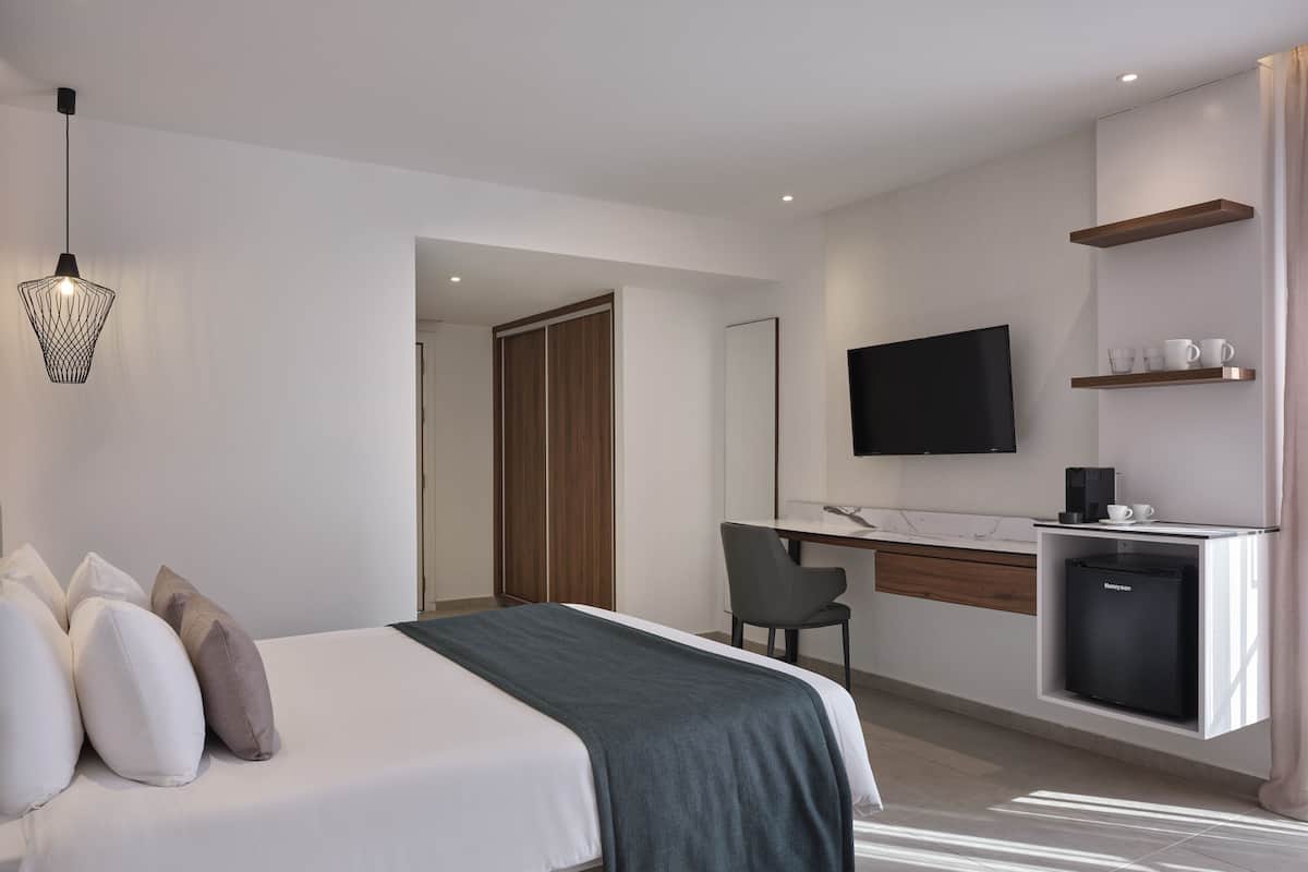 Una habitación de hotel moderna con cama, escritorio, silla, televisor y cafetera.