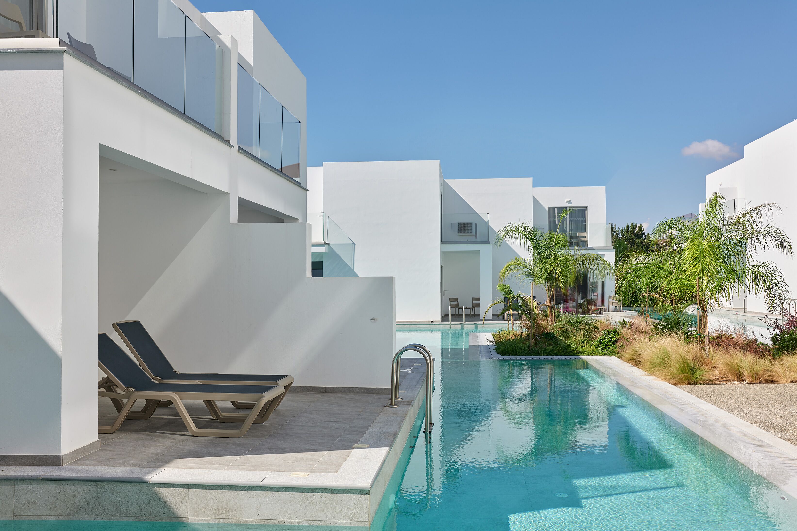 A modern pool area with lounge chairs, a clear pool, and white buildings.