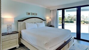 A large bed with white linens, a nightstand with a lamp, and a view of the outdoors through a glass door.