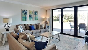 A modern living room with a grey sofa, a coffee table, and a large sliding glass door leading to an outdoor area.