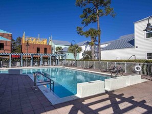 Une piscine dotée de chaises longues et d’un espace abrité, entourée d’immeubles et d’arbres.