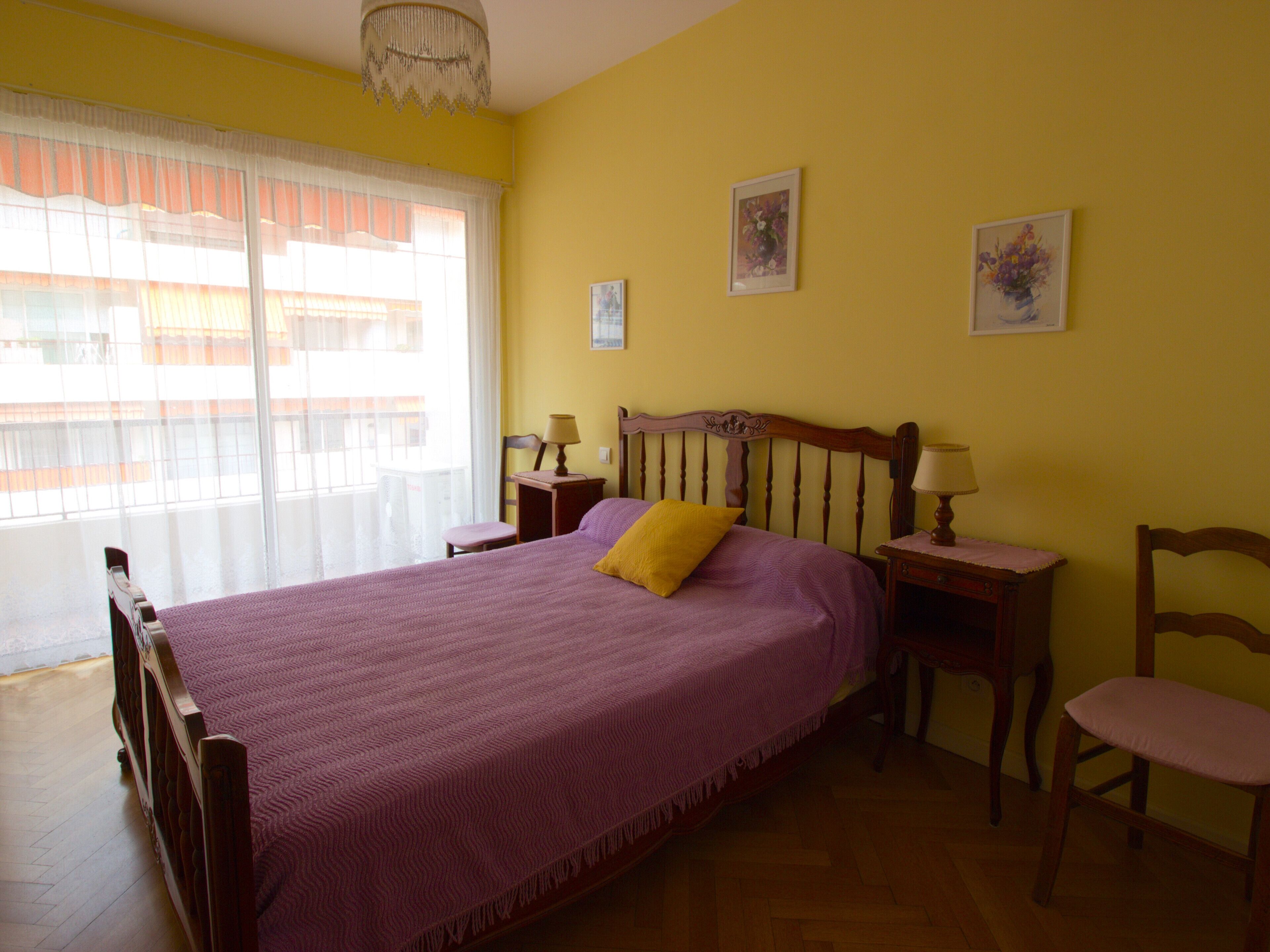 Un dormitorio con una cama grande, dos mesitas de noche, una silla y una ventana con cortinas de gasa.