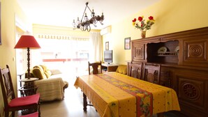 Un coin repas avec une table recouverte d’une nappe jaune, des chaises en bois, un lustre et un buffet orné d’assiettes décoratives.