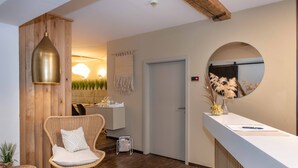 A modern reception area with a wooden accent wall, a round mirror, a wicker chair, and a reception desk. - Hotel Fuchs (Saarbrücken)