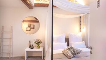 Quarto com cama de dossel, espelho redondo, mesa de cabeceira e parede de pedra.