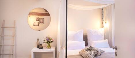 A bedroom with a canopy bed, a round mirror, a bedside table, and a stone wall.