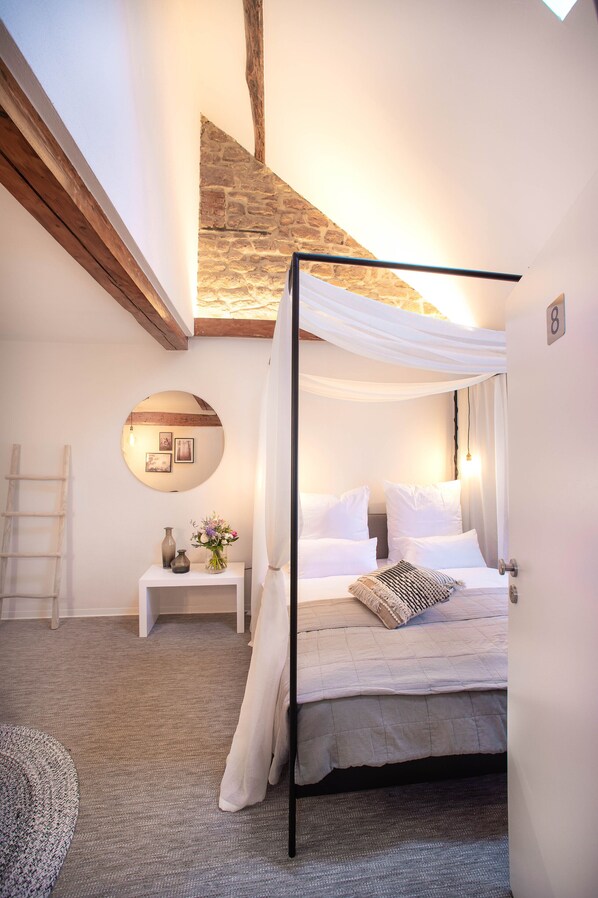 A bedroom with a canopy bed, a round mirror, a bedside table, and a stone wall. - Hotel Fuchs (Saarbrücken)