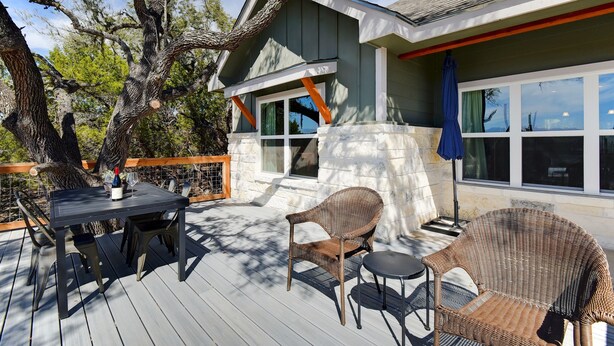 A deck with a table and chairs, a covered area with a blue umbrella, and a building with large windows. - Experience hill country life & relax! Family & Pet Friendly near Canyon Lake. (Canyon Lake)