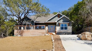 A two-story house with a garage, a front yard with a gravel path, and a large tree. - Experience hill country life & relax! Family & Pet Friendly near Canyon Lake. (Canyon Lake)