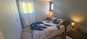 A bedroom with a bed, two bedside tables with lamps, a window with curtains, and a radiator.