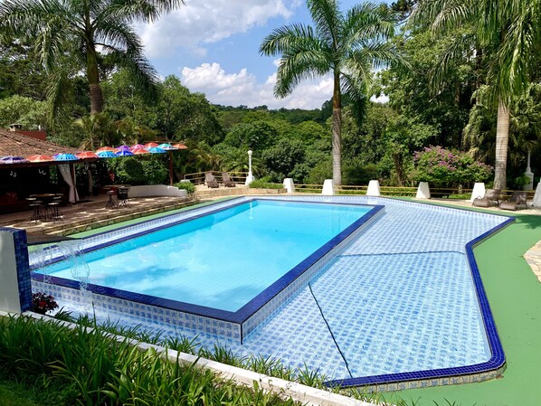 Ein rechteckiger Pool mit blauen Fliesen und einer umlaufenden, grünen Terrasse.