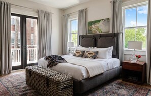 Un dormitorio con una cama grande, una mesita de noche, una lámpara, un cuadro y vistas al exterior.