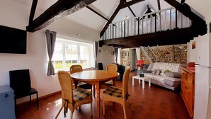 A cozy dining area with a wooden table and chairs, a stone wall, and a view of the garden through large windows. - "La Beuvrequentoise 2" just a stone's throw from Boulogne sur mer with NAUSICCA, Wissant  (Beuvrequen)