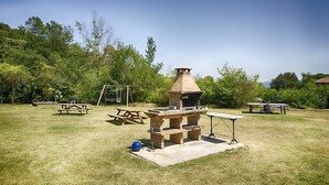 An outdoor barbecue area with a stone chimney, picnic tables, and a swing set.