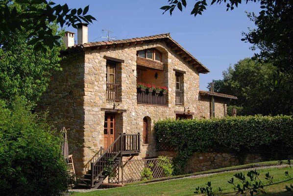 A stone house with a balcony, a wooden staircase, and a garden.
