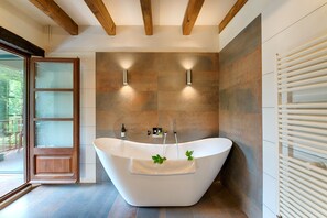 A modern bathroom with a freestanding bathtub, two wall-mounted lights, and a glass door leading to an outdoor area.