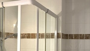 A shower enclosure with a glass door, a toilet, and a shelf with a plant and a basket. - Grenache (Collioure)
