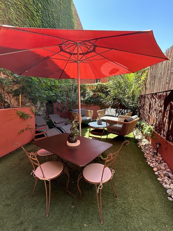 A patio with a table and chairs, a red umbrella, and a small potted plant.