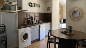 A compact kitchen with modern appliances, a dining area, and a stone wall. - Grenache (Collioure)