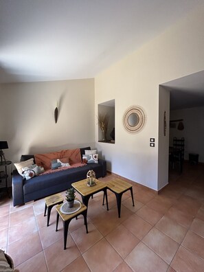 A living room with a sofa, two small tables, and a coffee table. There is a wall-mounted mirror and a decorative plate on the wall.