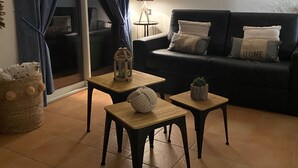 A living room with a dark-colored sofa, two small wooden tables, a lamp, and a basket. - Grenache (Collioure)