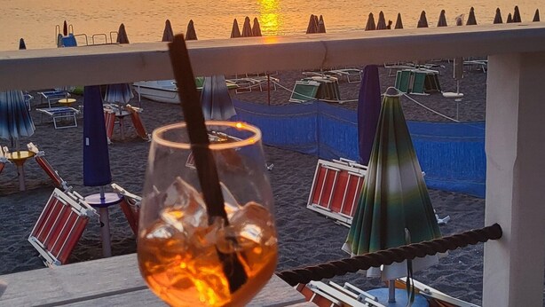 Zonsondergang zichtbaar vanaf een balkon, met een drankje en snacks op een tafel.