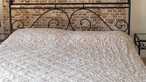 Een bed met een geborreld sprei, een achtergrond van een bakstenen muur en een hangende lamp.